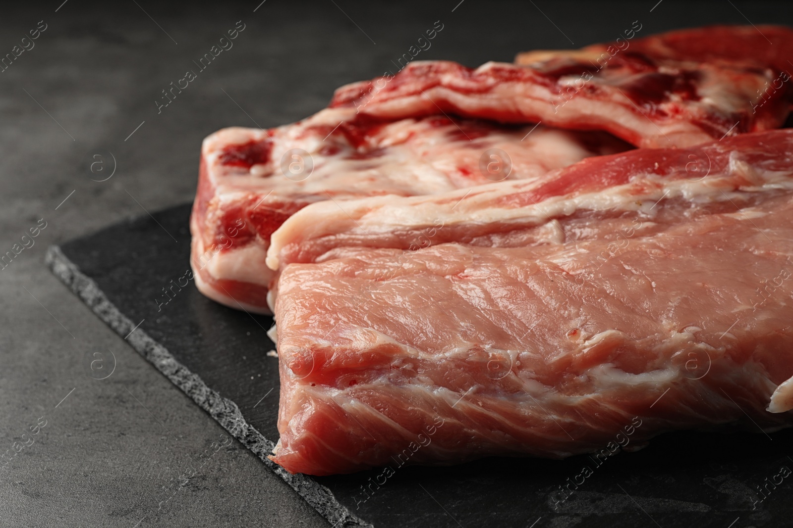 Photo of Slate plate with raw meat on grey table, closeup