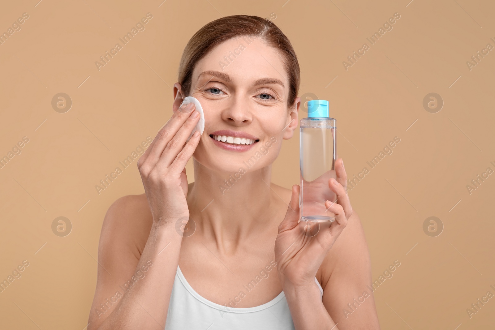 Photo of Beautiful woman removing makeup with cotton pad on beige background
