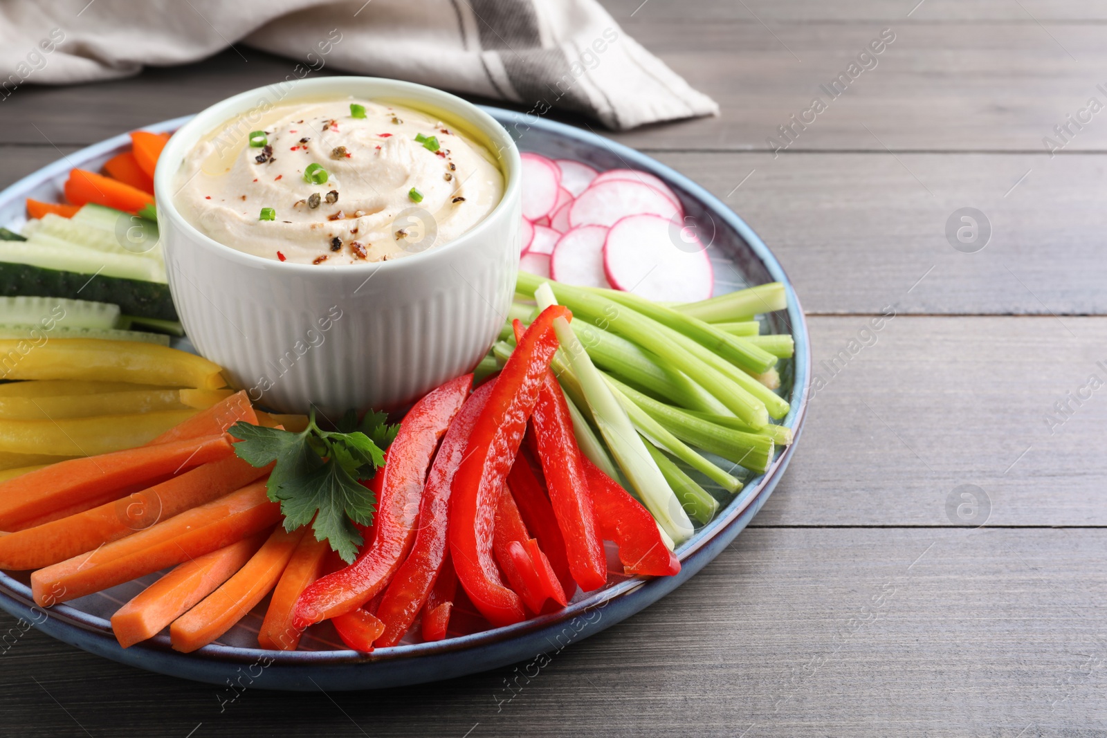 Photo of Fresh raw vegetable sticks and sauce on grey wooden table