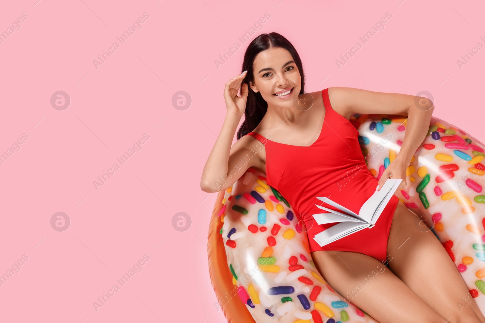 Photo of Young woman with book on inflatable ring against pink background, above view. Space for text