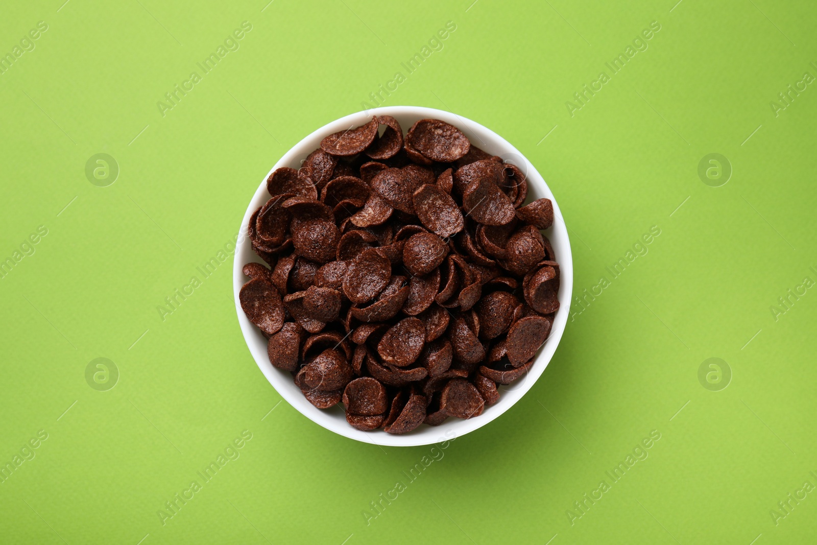 Photo of Breakfast cereal. Chocolate corn flakes in bowl on green table, top view