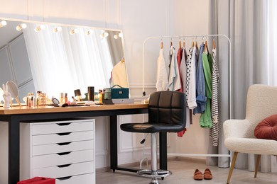 Makeup room. Stylish dressing table with mirror, chair and clothes rack