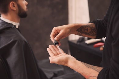 Photo of Hairdresser with beard serum near client in barbershop. Professional shaving service