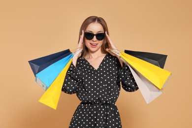 Stylish young woman in sunglasses with shopping bags on beige background