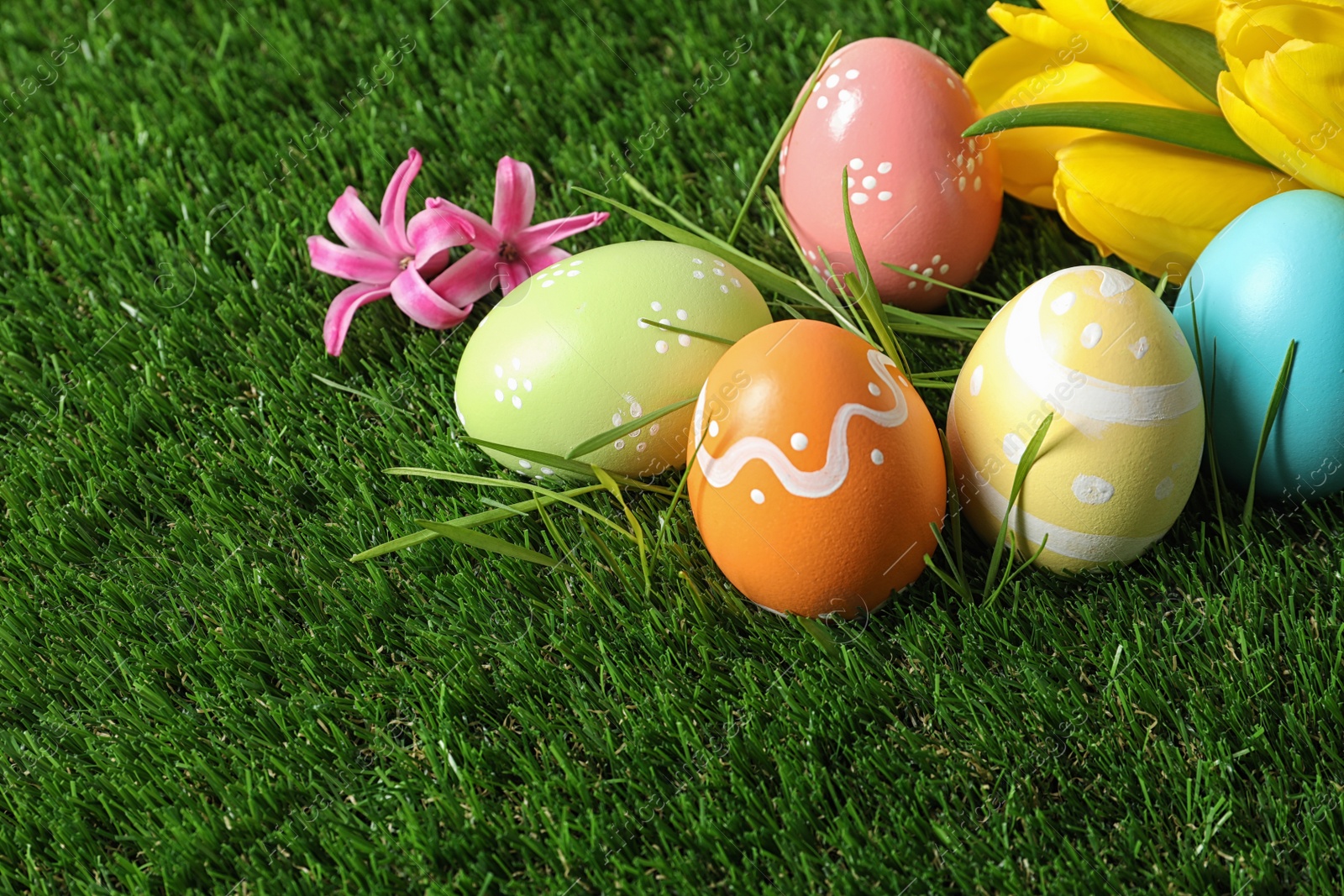 Photo of Colorful painted Easter eggs and flowers on green grass, space for text