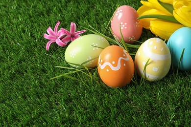 Colorful painted Easter eggs and flowers on green grass, space for text