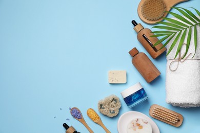 Flat lay composition with different spa products and tropical leaf on light blue background. Space for text