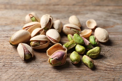 Photo of Many organic pistachio nuts on wooden table