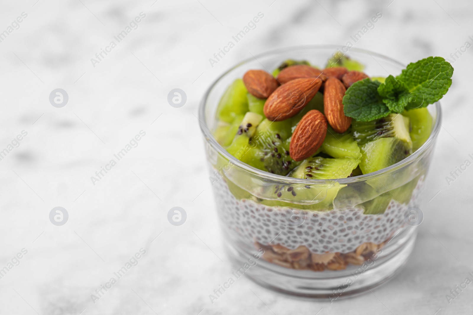 Photo of Delicious dessert with kiwi, chia seeds and almonds on white table, closeup. Space for text