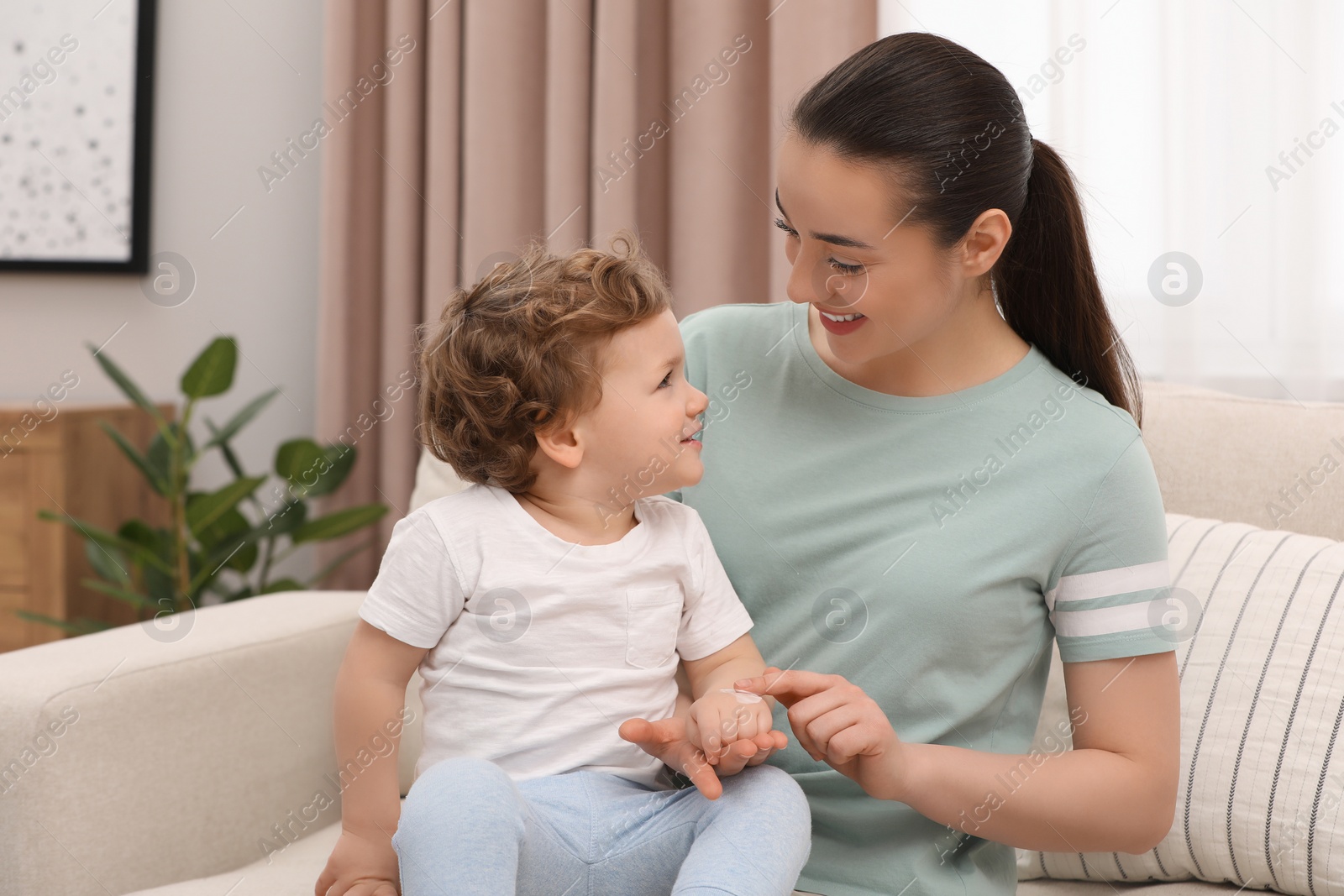 Photo of Mother applying ointment onto her son`s hand on sofa at home