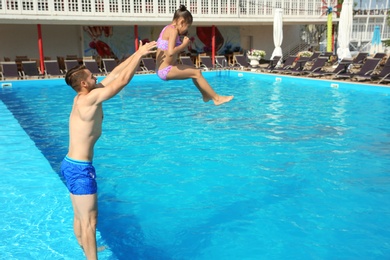 Photo of Young father playing with little daughter in swimming pool on sunny day