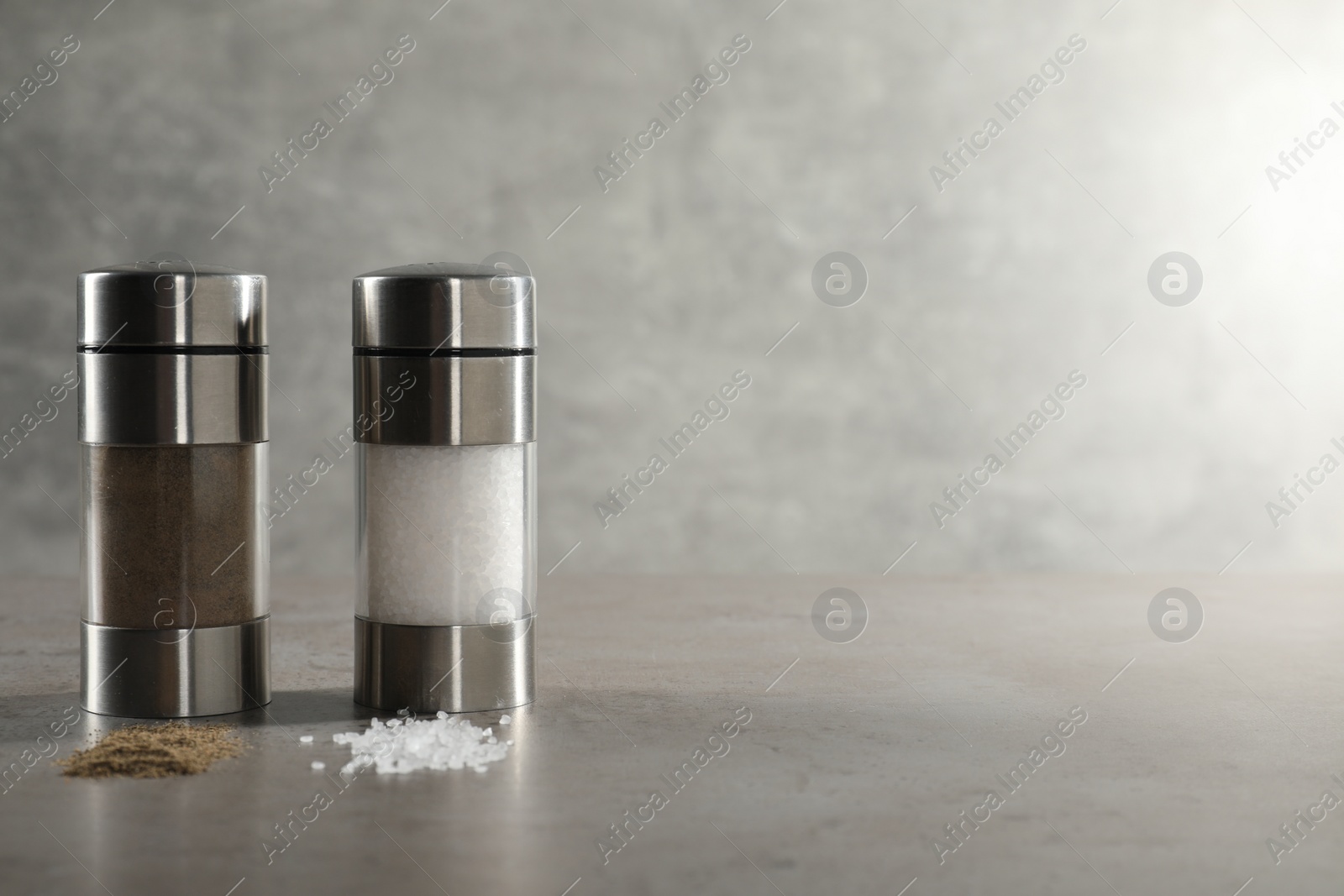 Photo of Salt and pepper shakers on grey textured table, closeup. Space for text