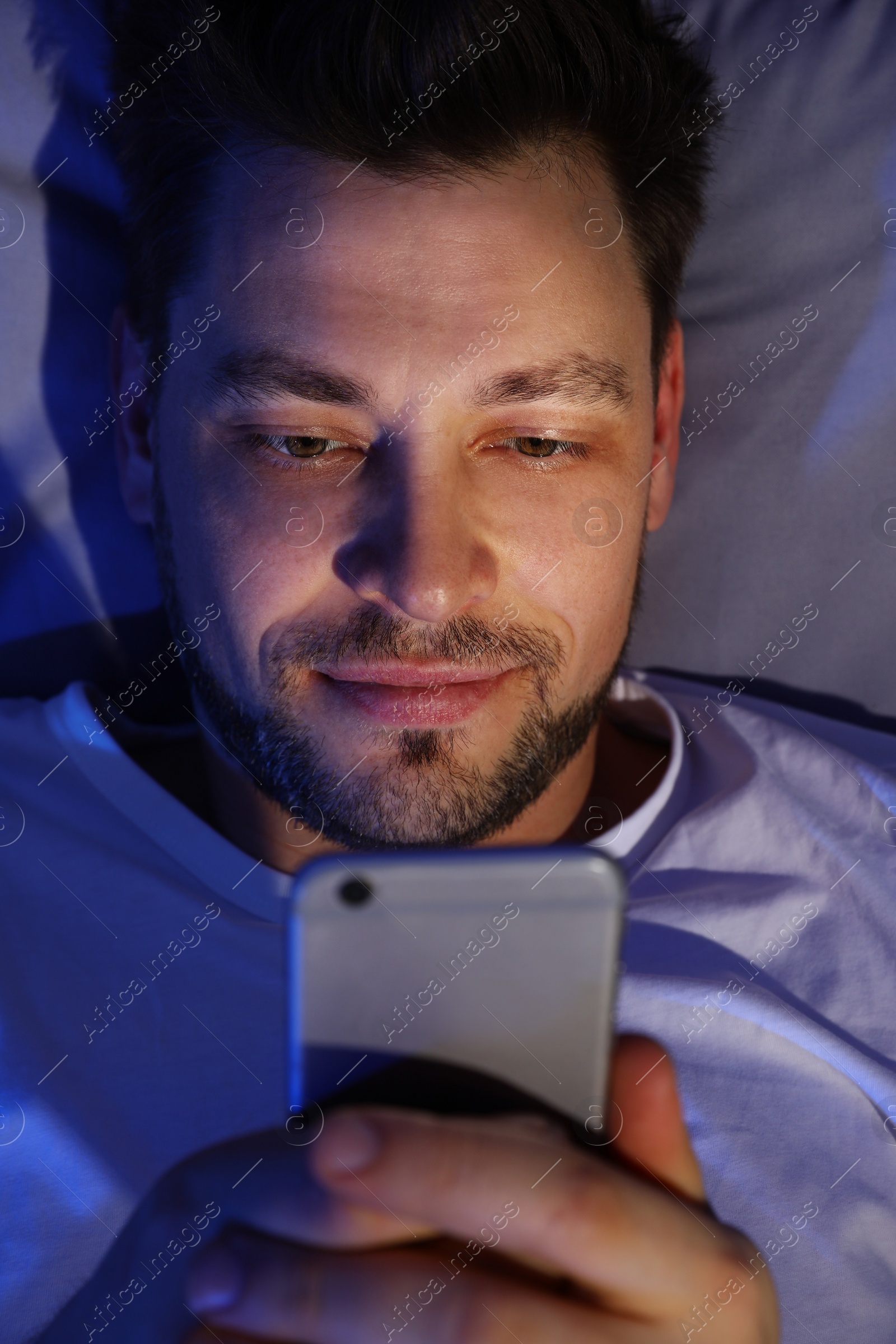 Photo of Handsome man using smartphone at night, view from above. Bedtime