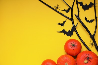 Flat lay composition with black branches, paper bats and pumpkins on yellow background, space for text. Halloween celebration