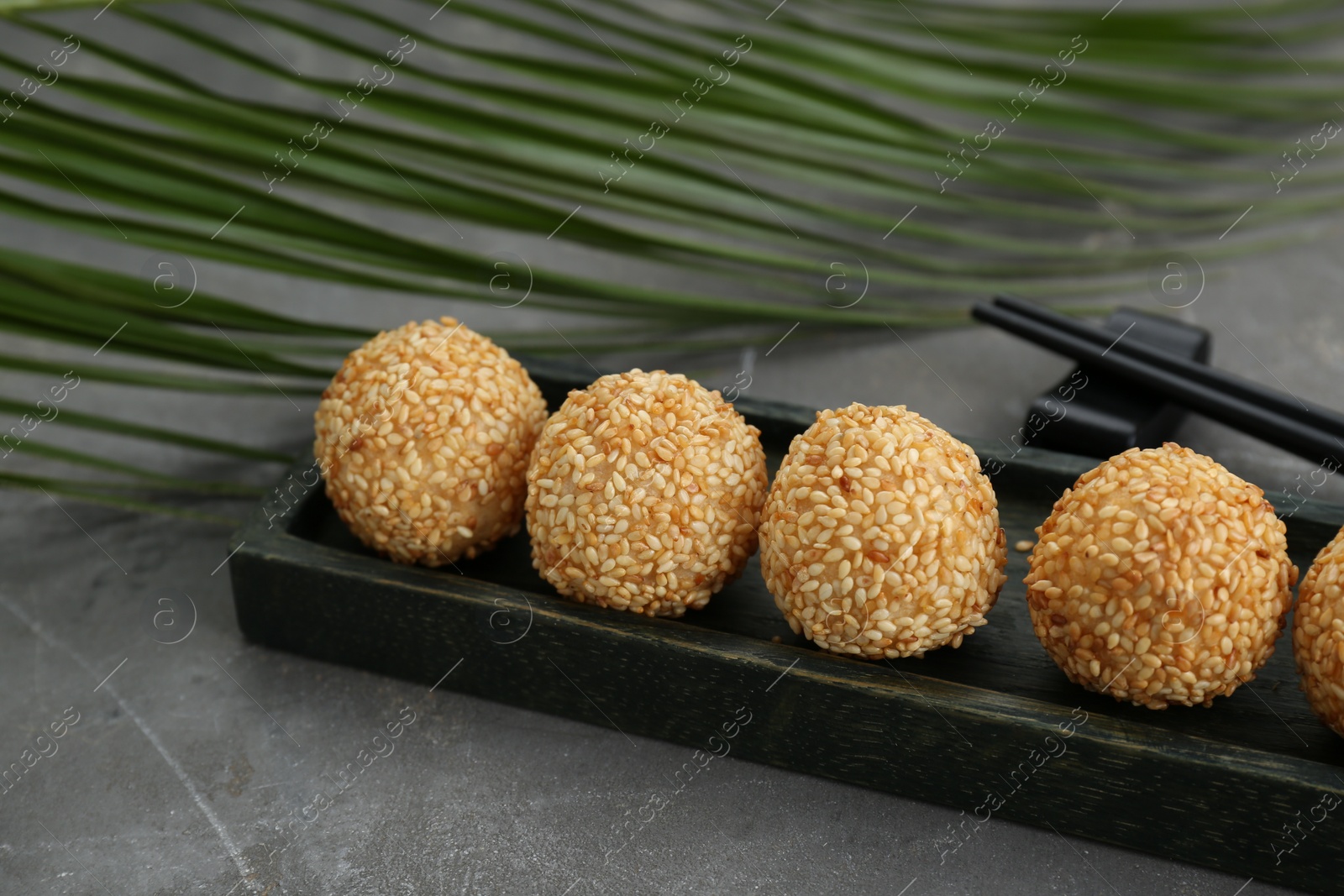 Photo of Delicious sesame balls and green leaf on grey table