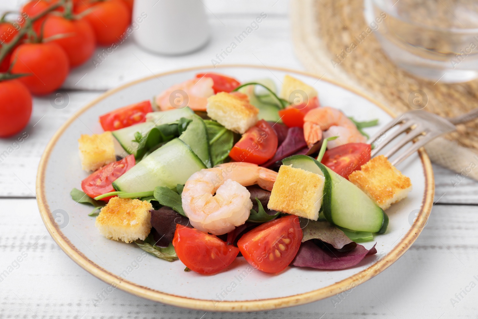 Photo of Tasty salad with croutons, tomato and shrimps served on white wooden table, closeup