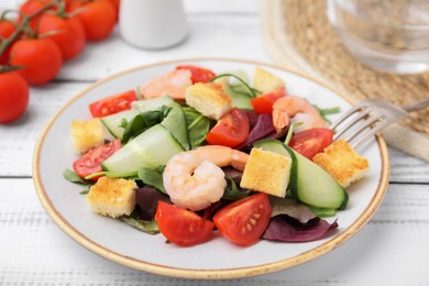 Photo of Tasty salad with croutons, tomato and shrimps served on white wooden table, closeup