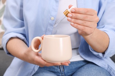 Photo of Woman dripping food supplement into cup indoors, closeup