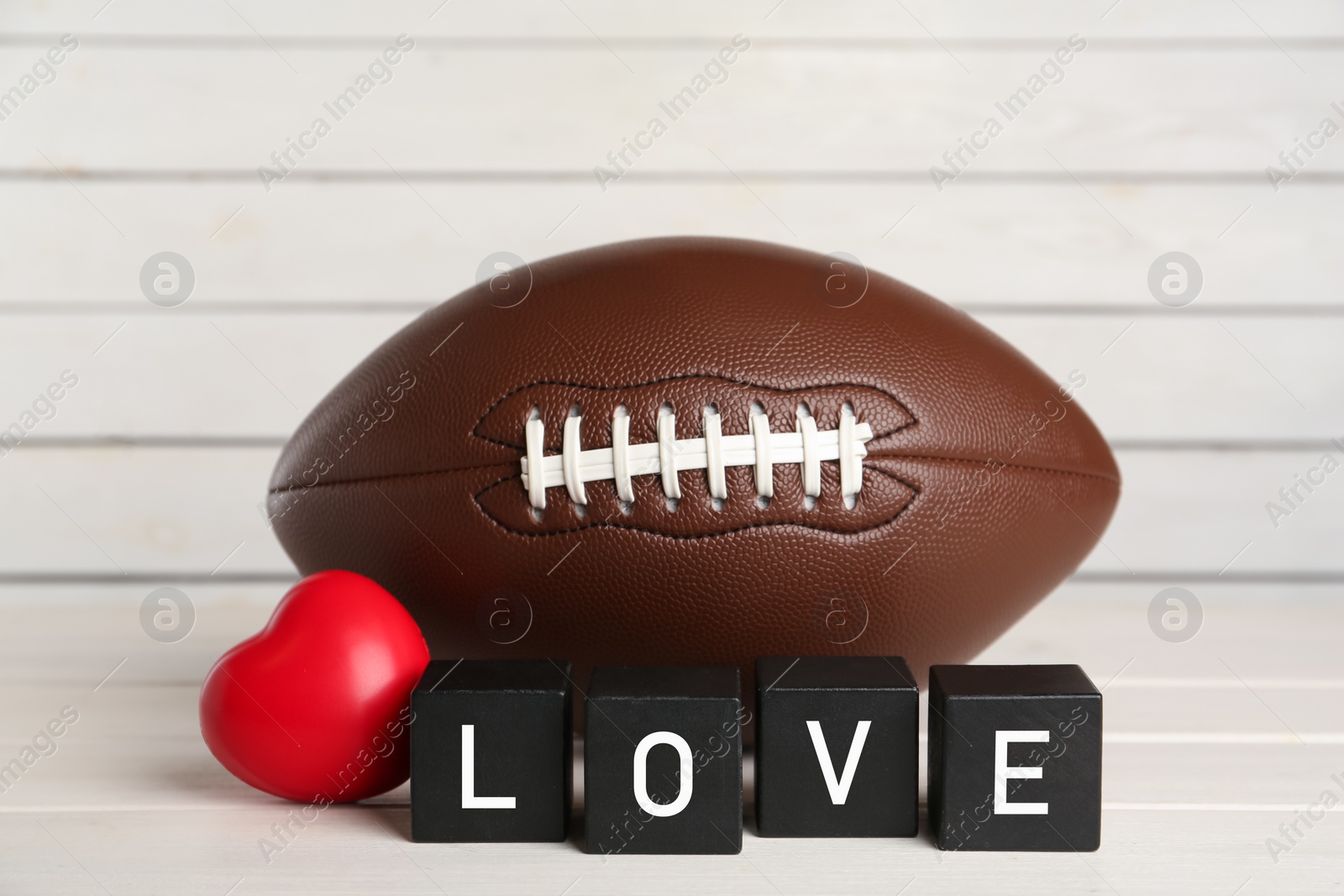 Photo of American football ball, heart and cubes with word Love on white wooden table