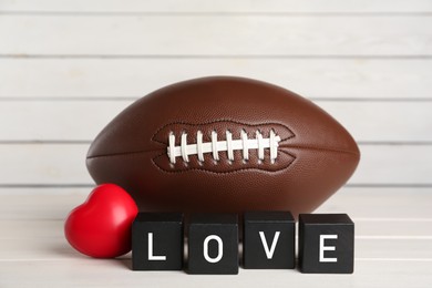 American football ball, heart and cubes with word Love on white wooden table