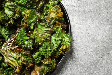 Tasty baked kale chips on grey table, top view