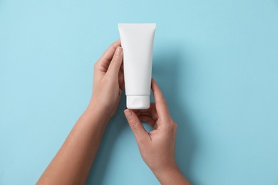 Woman with tube of hand cream on light blue background, top view