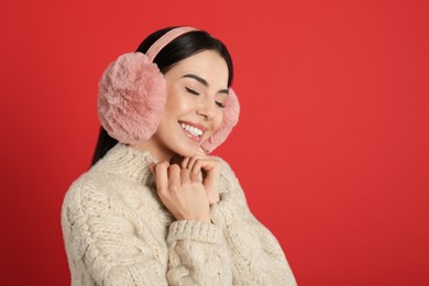 Photo of Beautiful young woman wearing earmuffs on red background. Space for text
