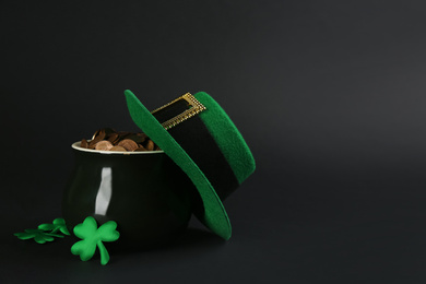 Photo of Pot of gold coins, hat and clover leaves on black background, space for text. St. Patrick's Day celebration