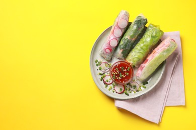 Delicious spring rolls served with sauce on yellow background, top view. Space for text