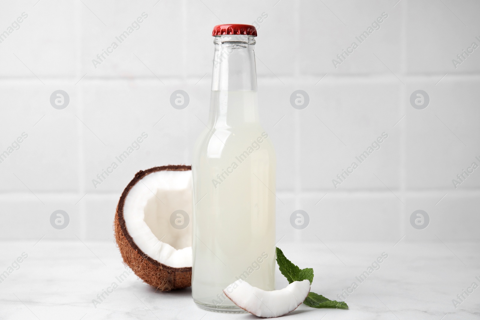 Photo of Delicious kombucha in glass bottle, coconut and mint on white marble table