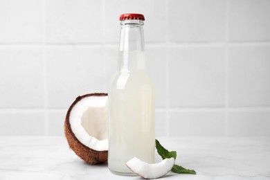 Photo of Delicious kombucha in glass bottle, coconut and mint on white marble table