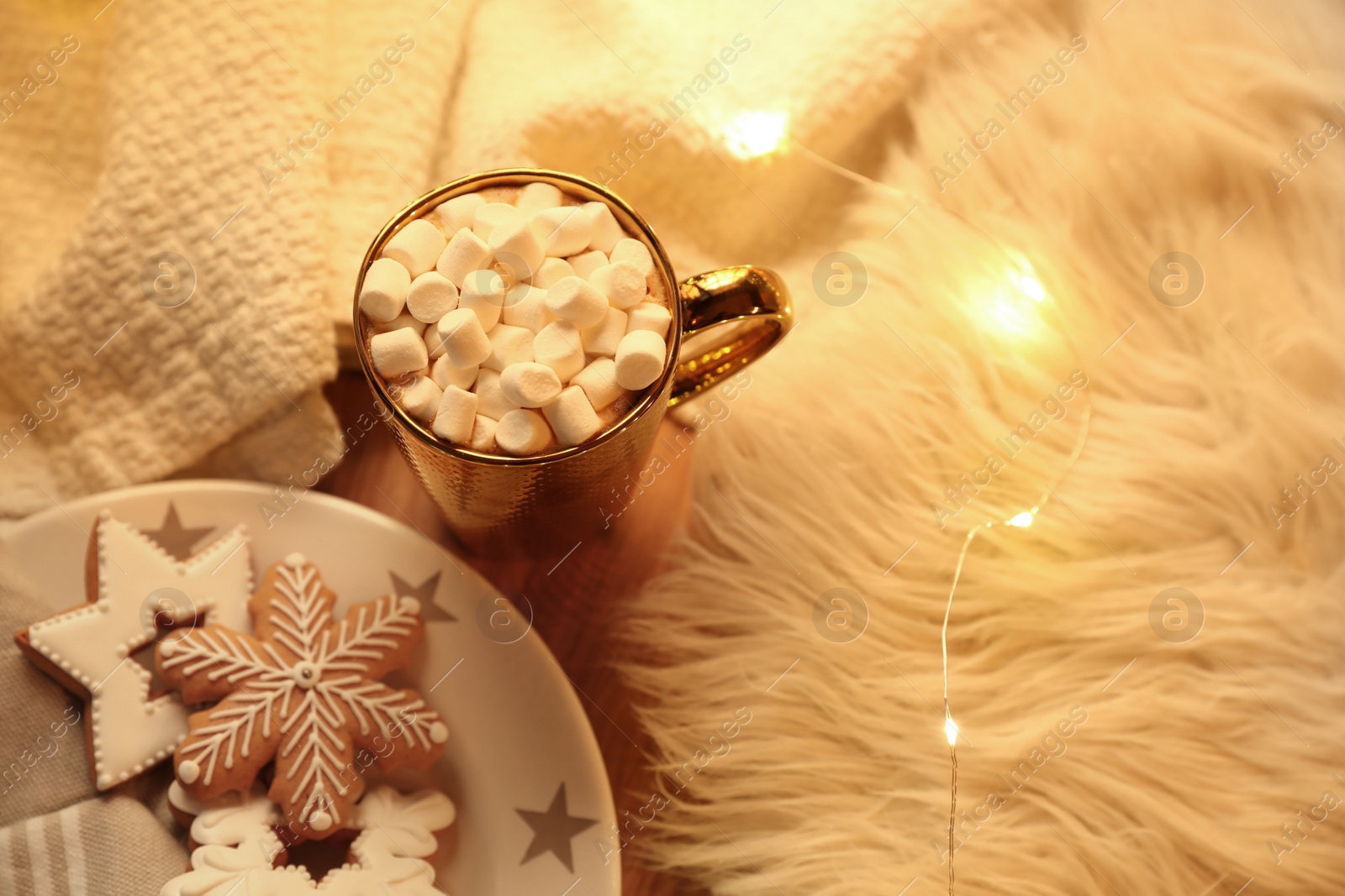 Photo of Cup of hot drink with marshmallows, cookies and Christmas lights on table, above view