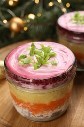 Photo of Glass jars with herring under fur coat and Christmas decor on wooden table, closeup. Traditional Russian salad