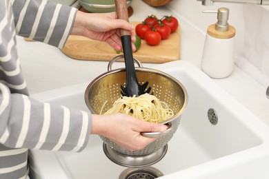 Photo of Woman with colander of cooked spaghetti and pasta server at sink, closeup
