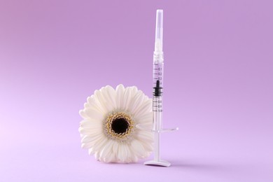 Cosmetology. Medical syringe and gerbera flower on violet background