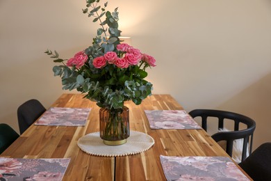 Photo of Beautiful bouquet of roses and eucalyptus branches in vase near napkins on wooden table indoors