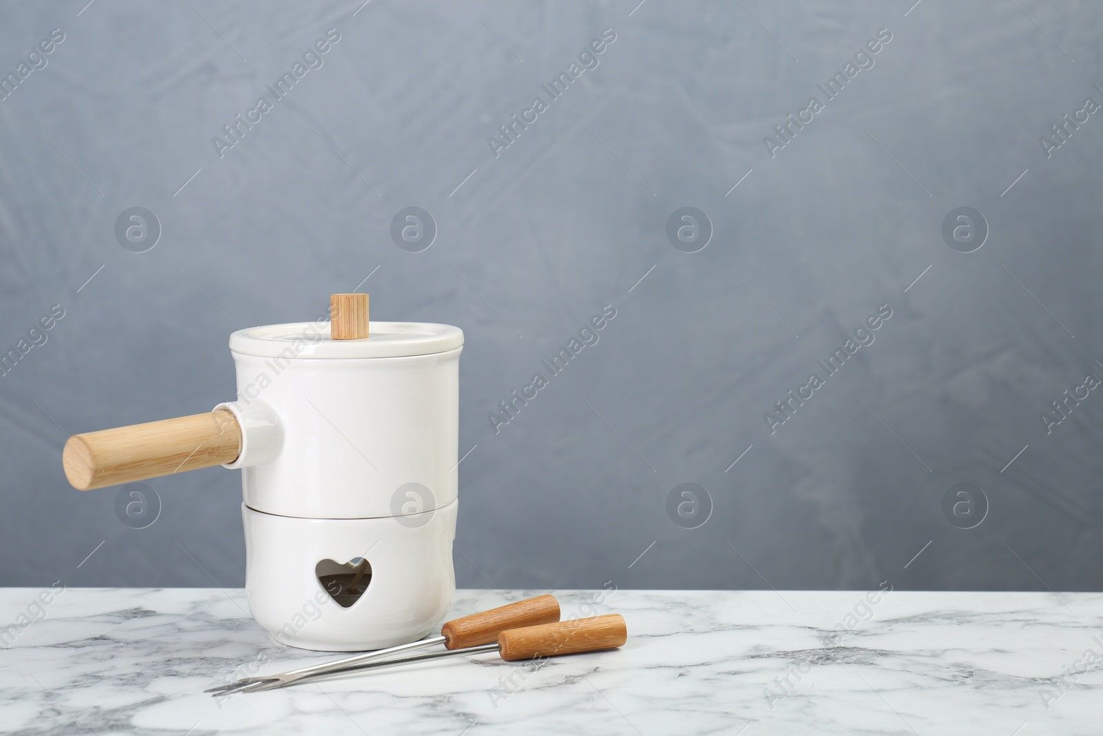 Photo of Fondue set on white marble table against light grey background, space for text