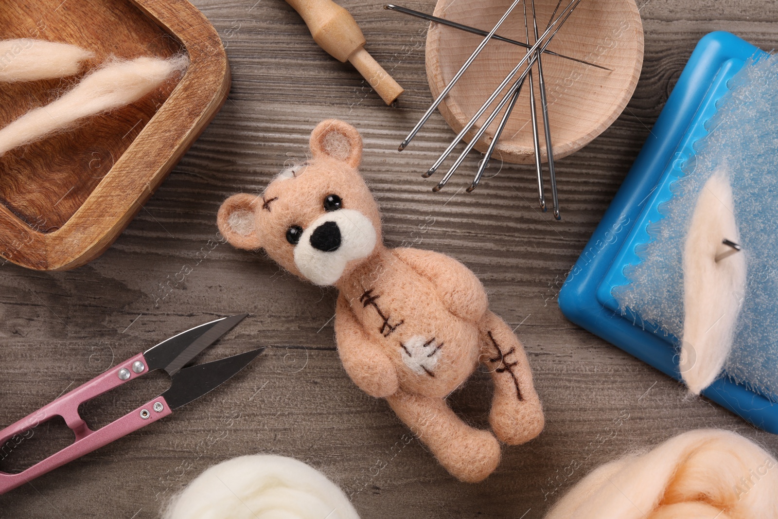 Photo of Felted bear, wool and different tools on wooden table, flat lay