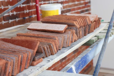 Photo of Many decorative bricks on scaffolding indoors. Tiles installation process