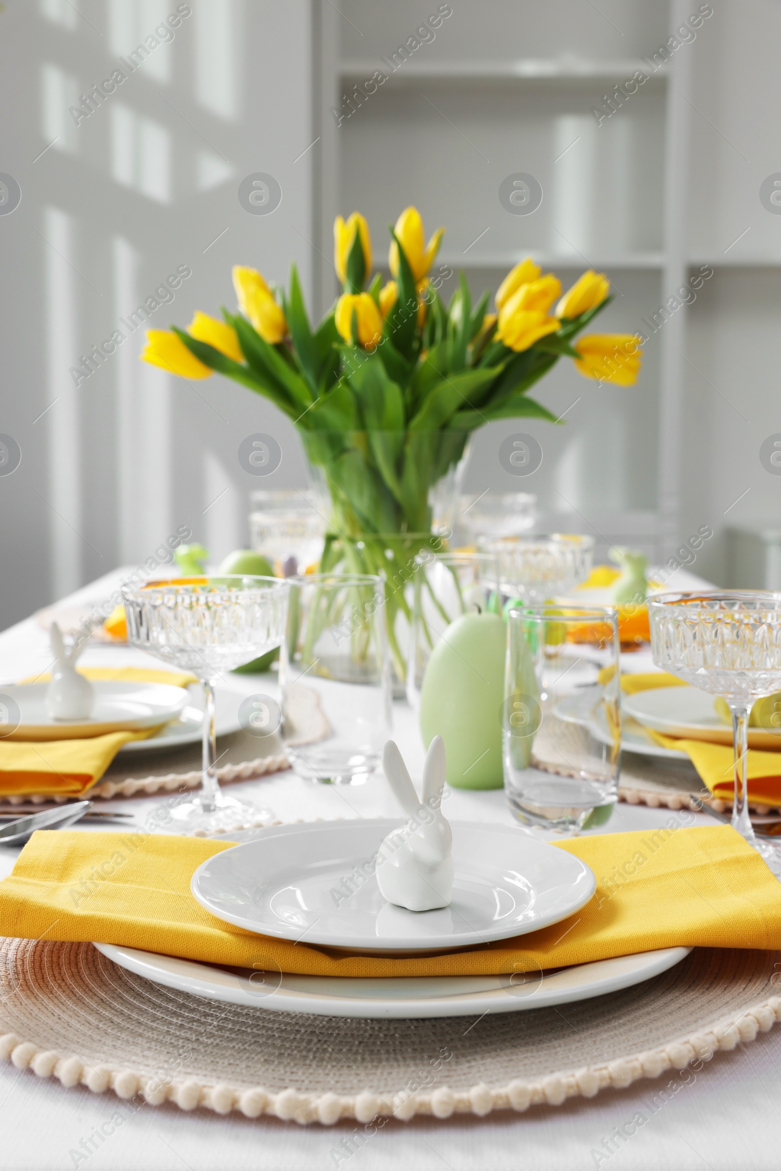 Photo of Festive table setting with glasses, painted eggs and vase of tulips. Easter celebration