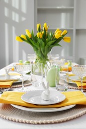 Photo of Festive table setting with glasses, painted eggs and vase of tulips. Easter celebration