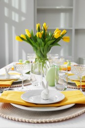 Festive table setting with glasses, painted eggs and vase of tulips. Easter celebration