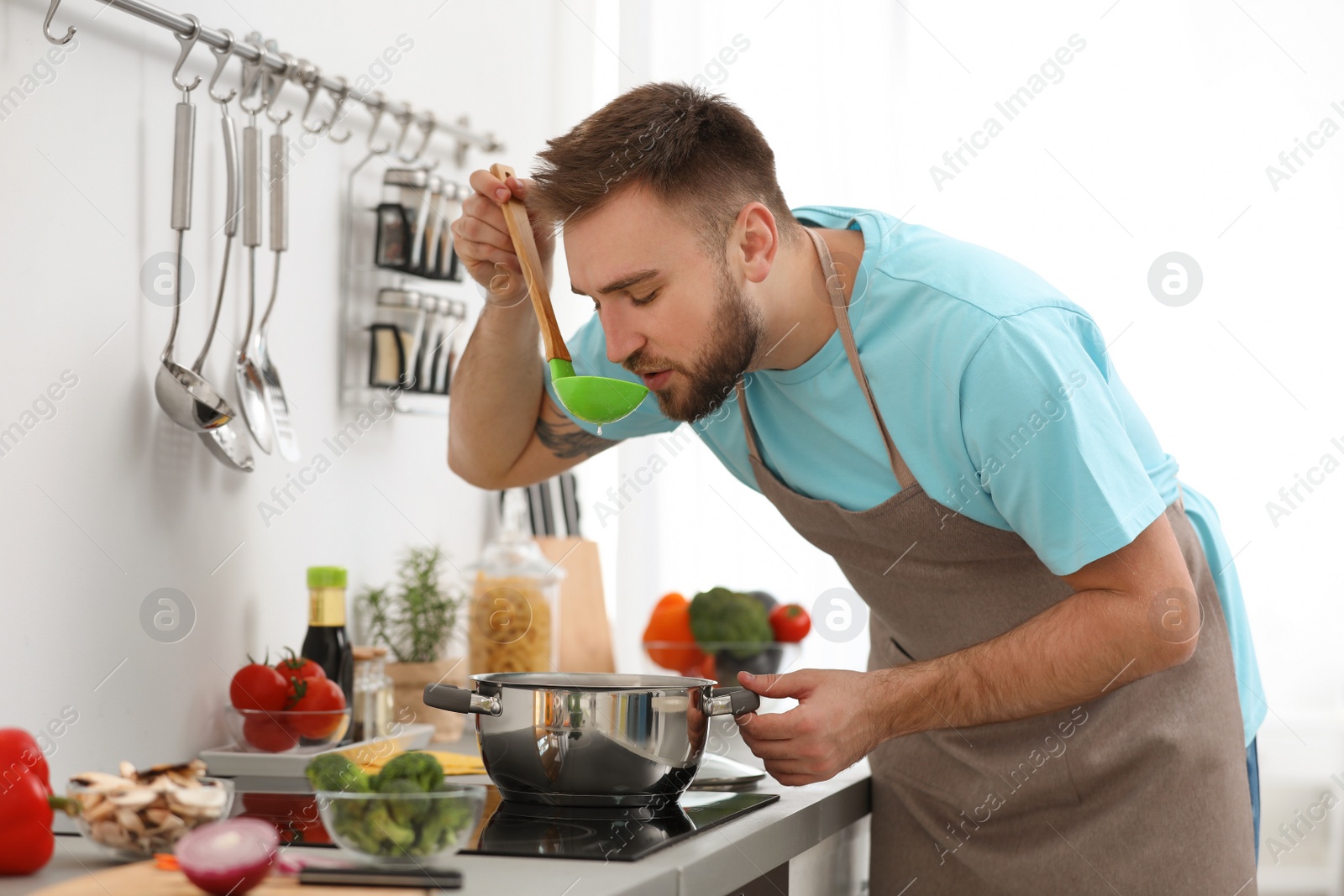 Photo of Young man cooking delicious soup in kitchen