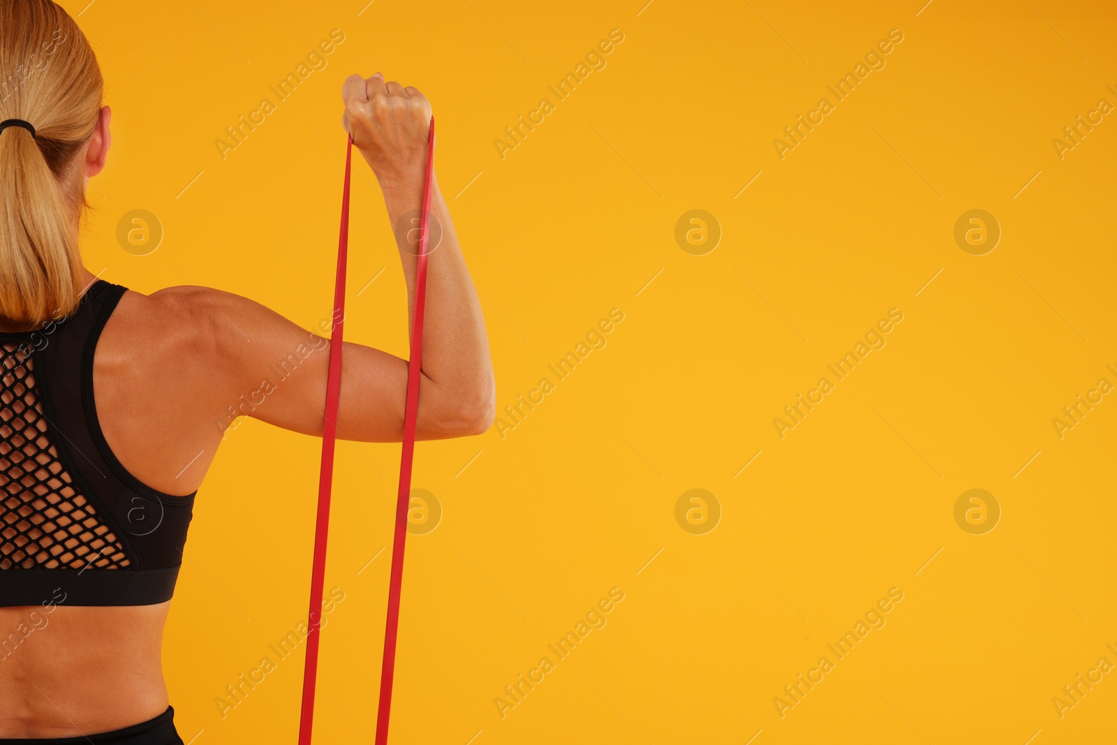 Photo of Woman exercising with elastic resistance band on orange background, back view. Space for text