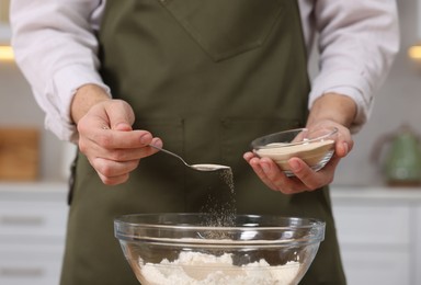 Photo of Making bread. Man putting dry yeast into bowl with flour in kitchen, closeup
