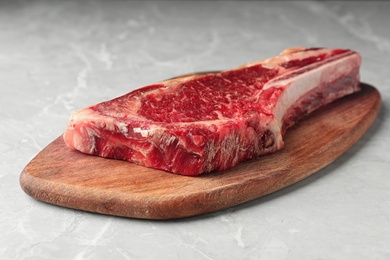 Wooden board with raw beef meat on light grey marble table, closeup