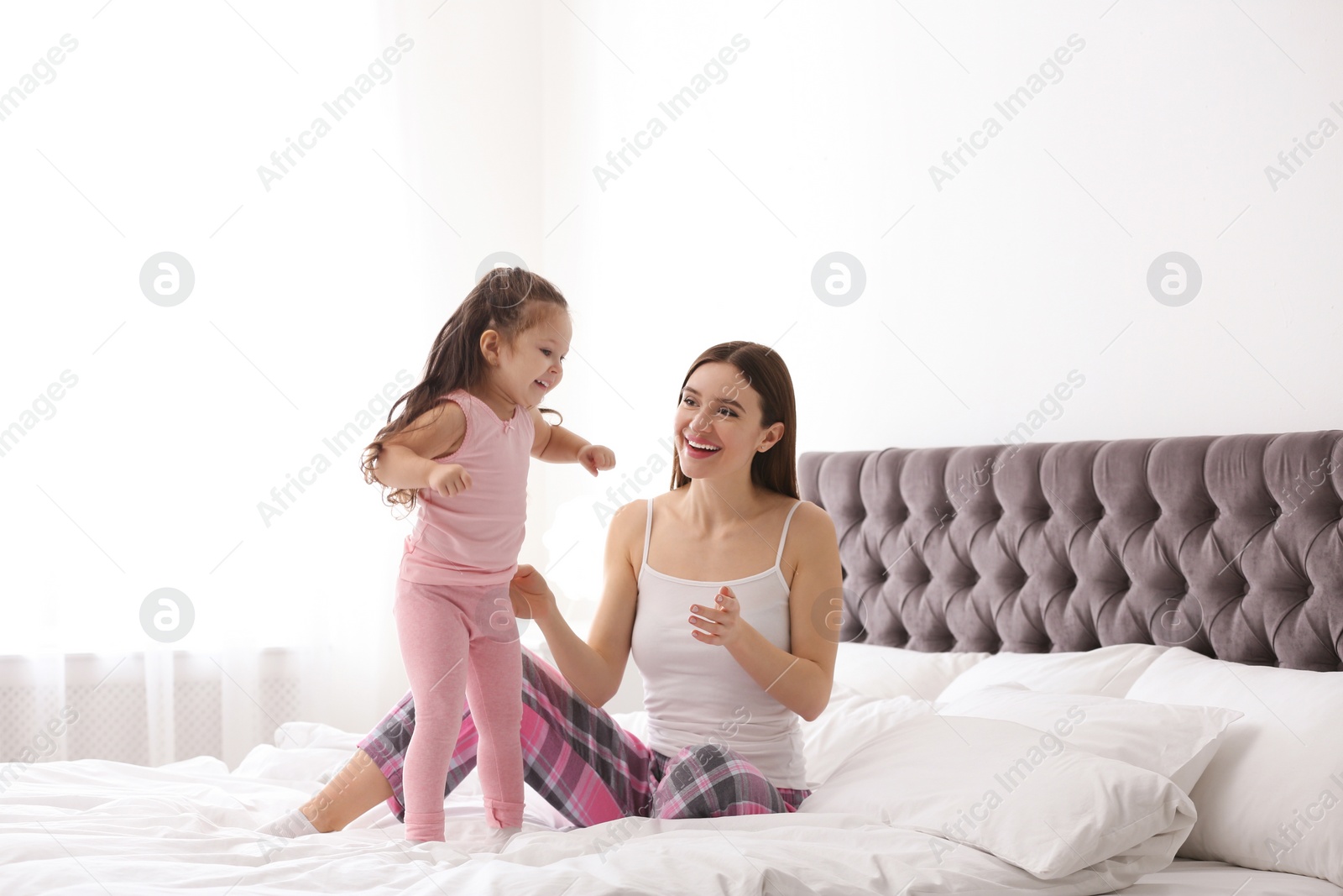 Photo of Happy mother with little daughter playing on bed