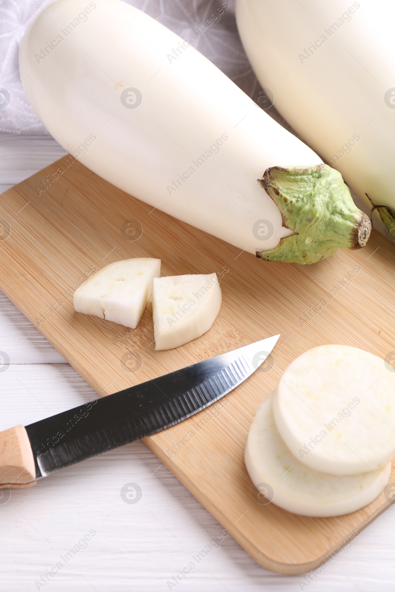 Photo of Board, raw white eggplants and knife on wooden table