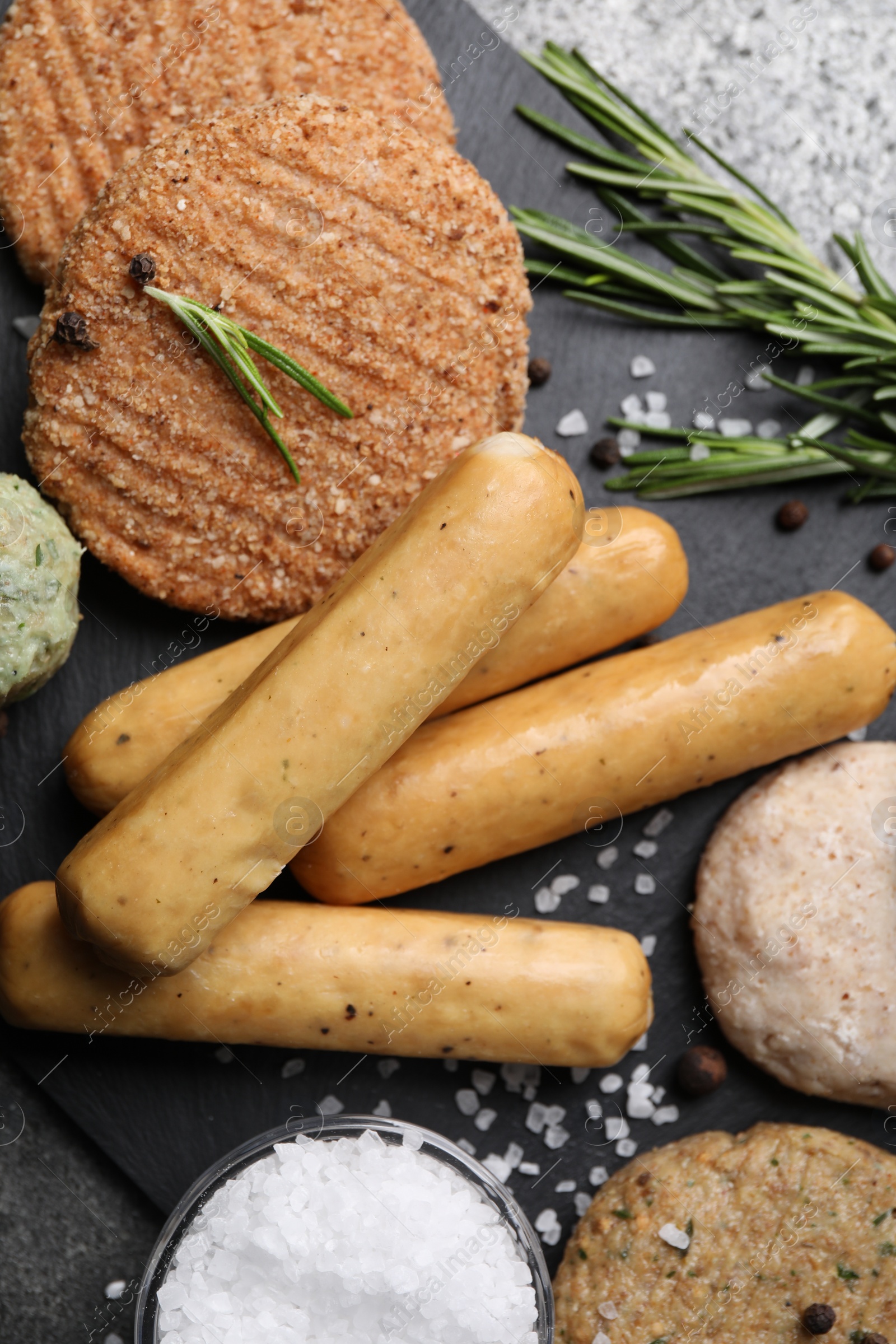 Photo of Different raw vegan meat products, salt and rosemary on dark board, flat lay