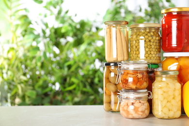 Photo of Glass jars of different pickled vegetables on light table. Space for text